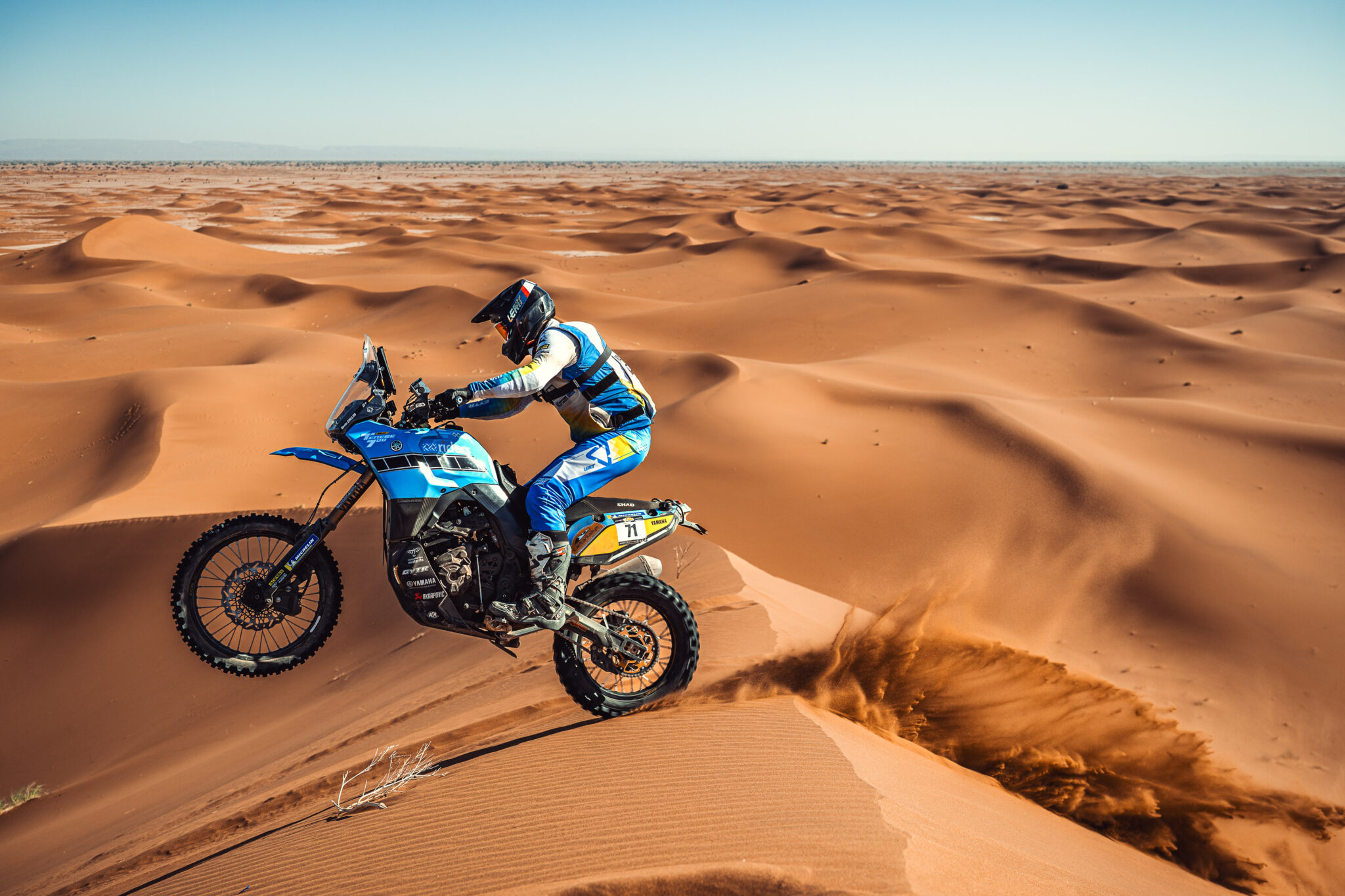 Rider on a blue Yamaha Ténéré 700 Rally on a dune crest in the desert