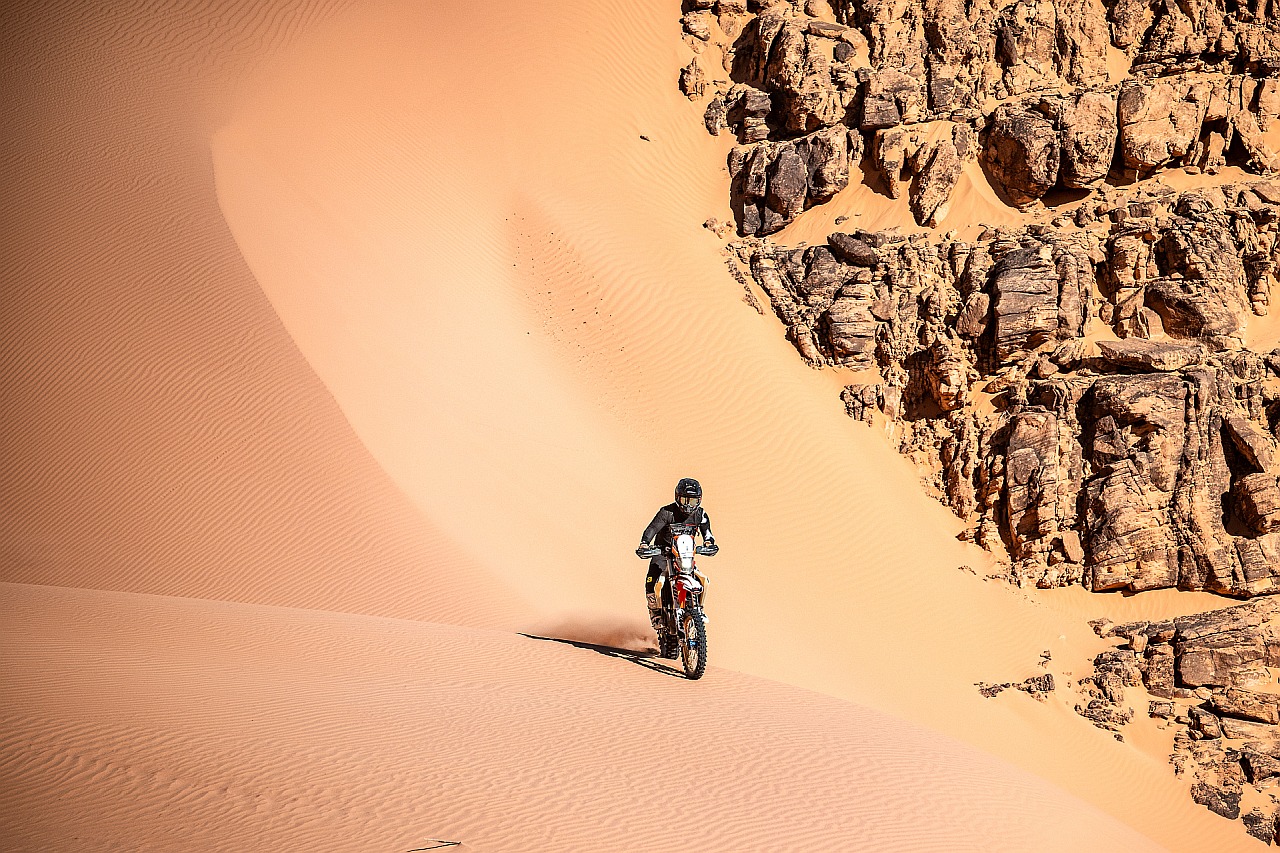 Motorcyclist on a sand dune in front of rocks in the desert