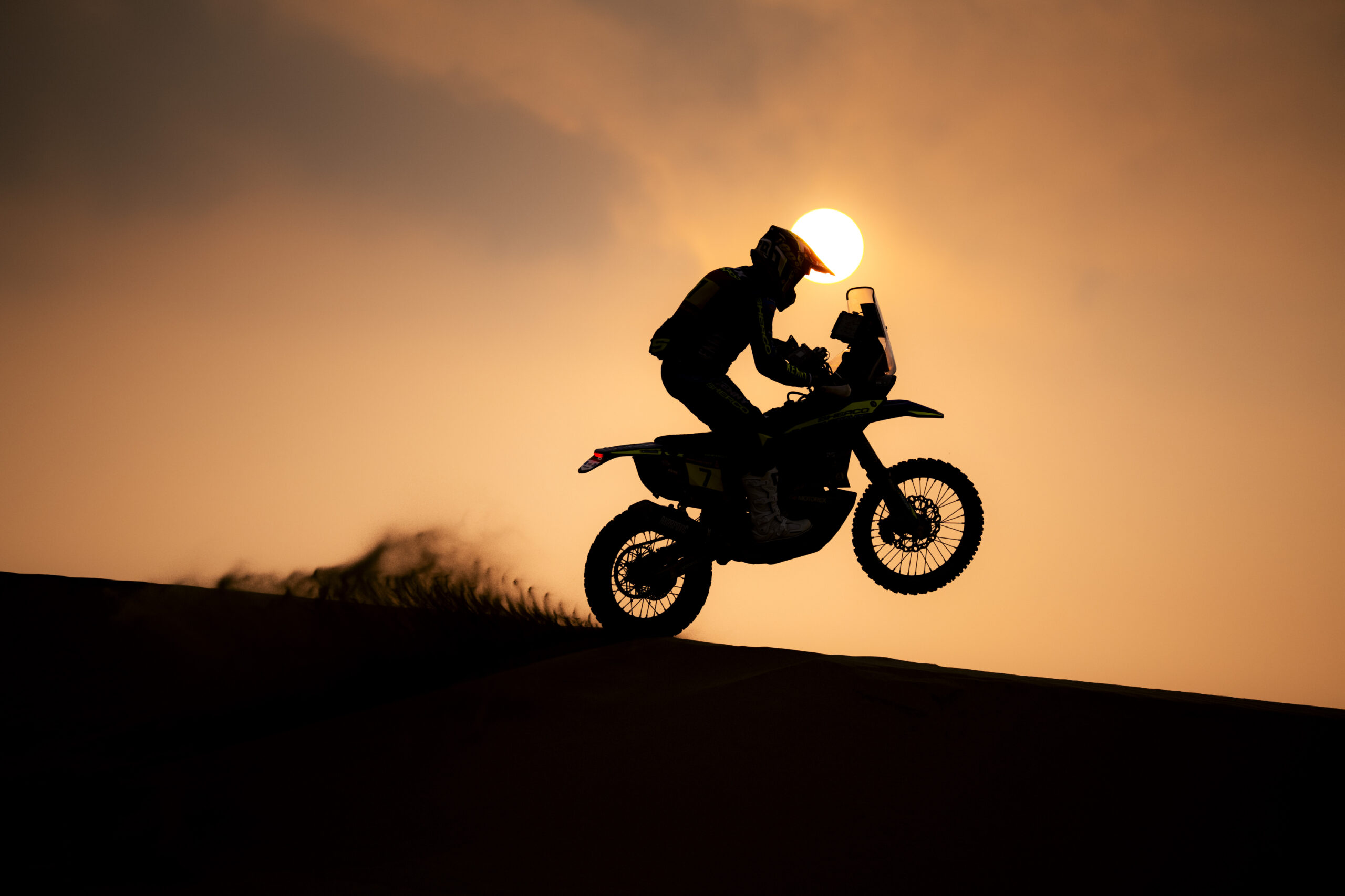 Silhouette of a rally rider on a dune in front of a low sun