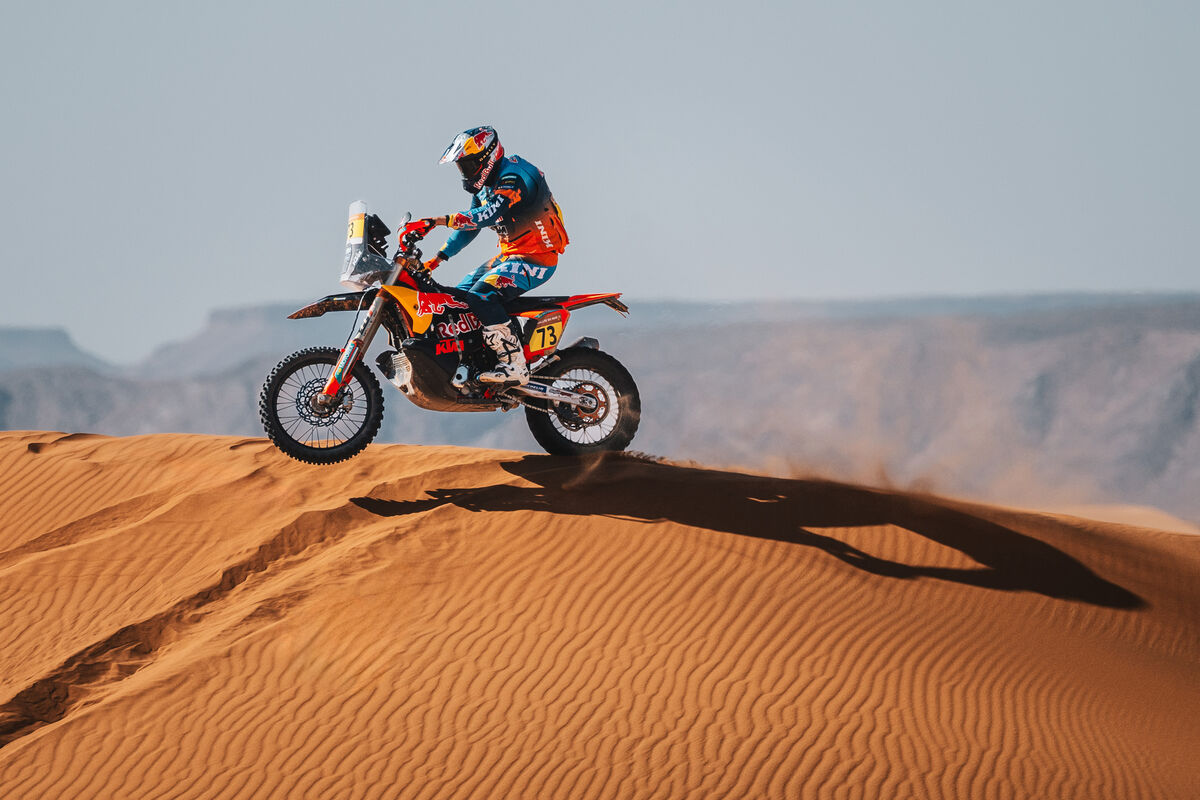 KTM rally rider with number 73 on the crest of a sand dune