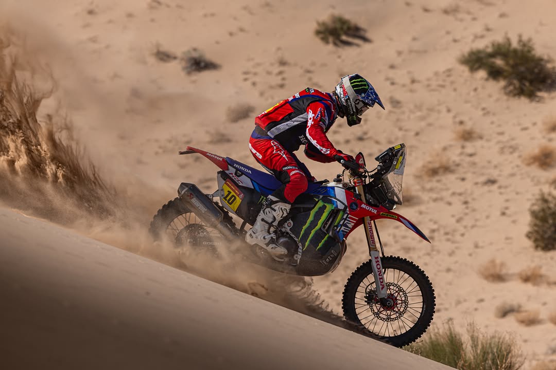 Motorcycle rally rider with number 10 climbing a sand dune and kicking up sand