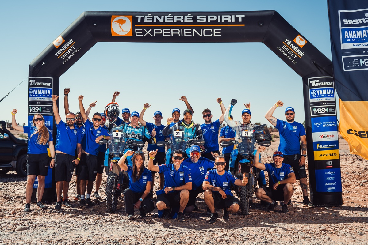 Fahrer und Mitarbeiter des Ténéré Yamaha Rally Team mit drei Ténéré 700 Rally unter einem Zielbogen in der Wüste
