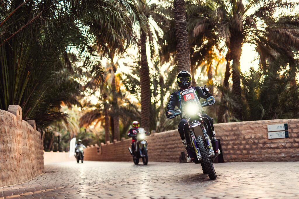 Rallye-Motorräder fahren mit Licht auf einem gepflasterten Weg durch die Palmenoase von Al Ain