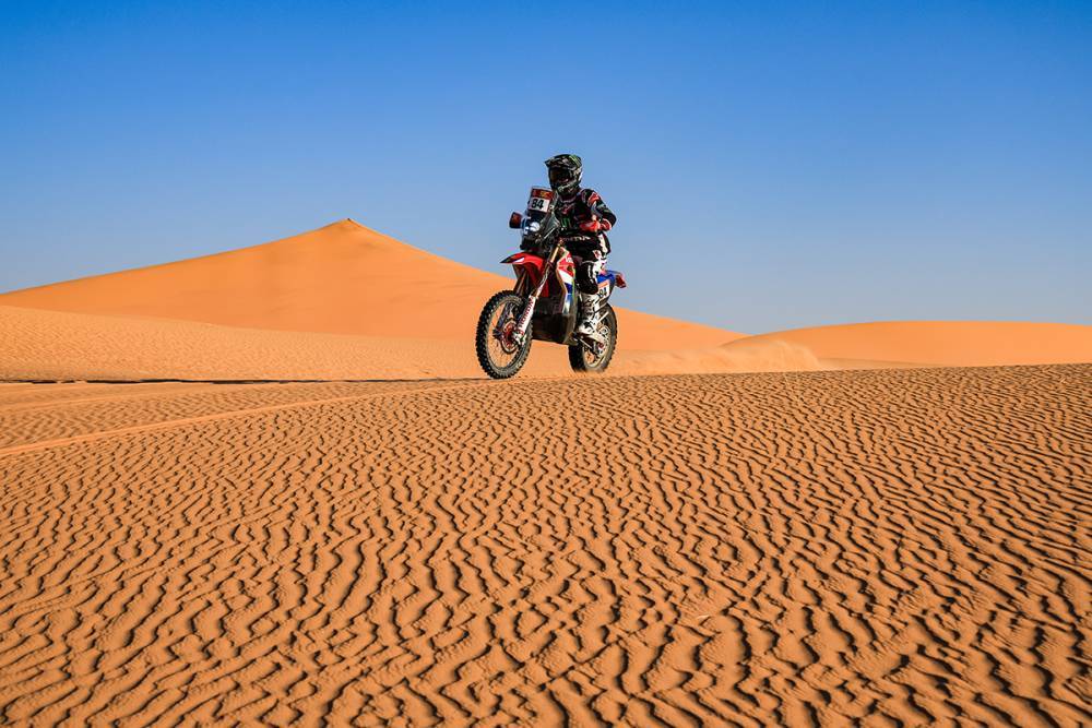 Rallye-Motorradfahrer fährt bei der Dakar 2026 durch Sanddünen unter blauem Himmel