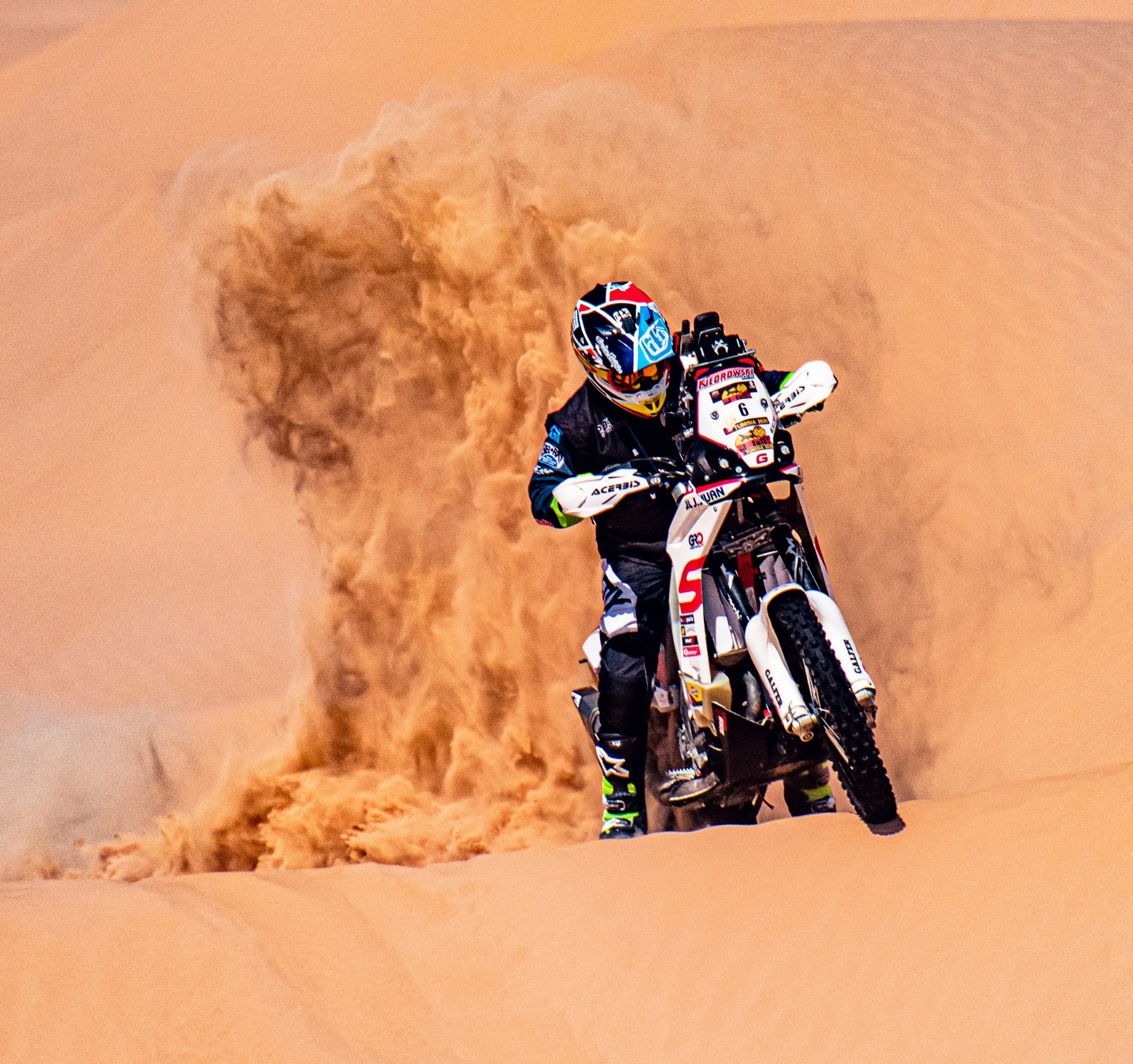 Rallye-Motorradfahrer mit Startnummer 6 f&auml;hrt durch eine Sandwolke in den D&uuml;nen