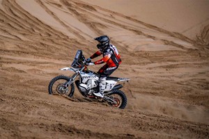 Motorcyclist in rally gear riding through a sand dune
