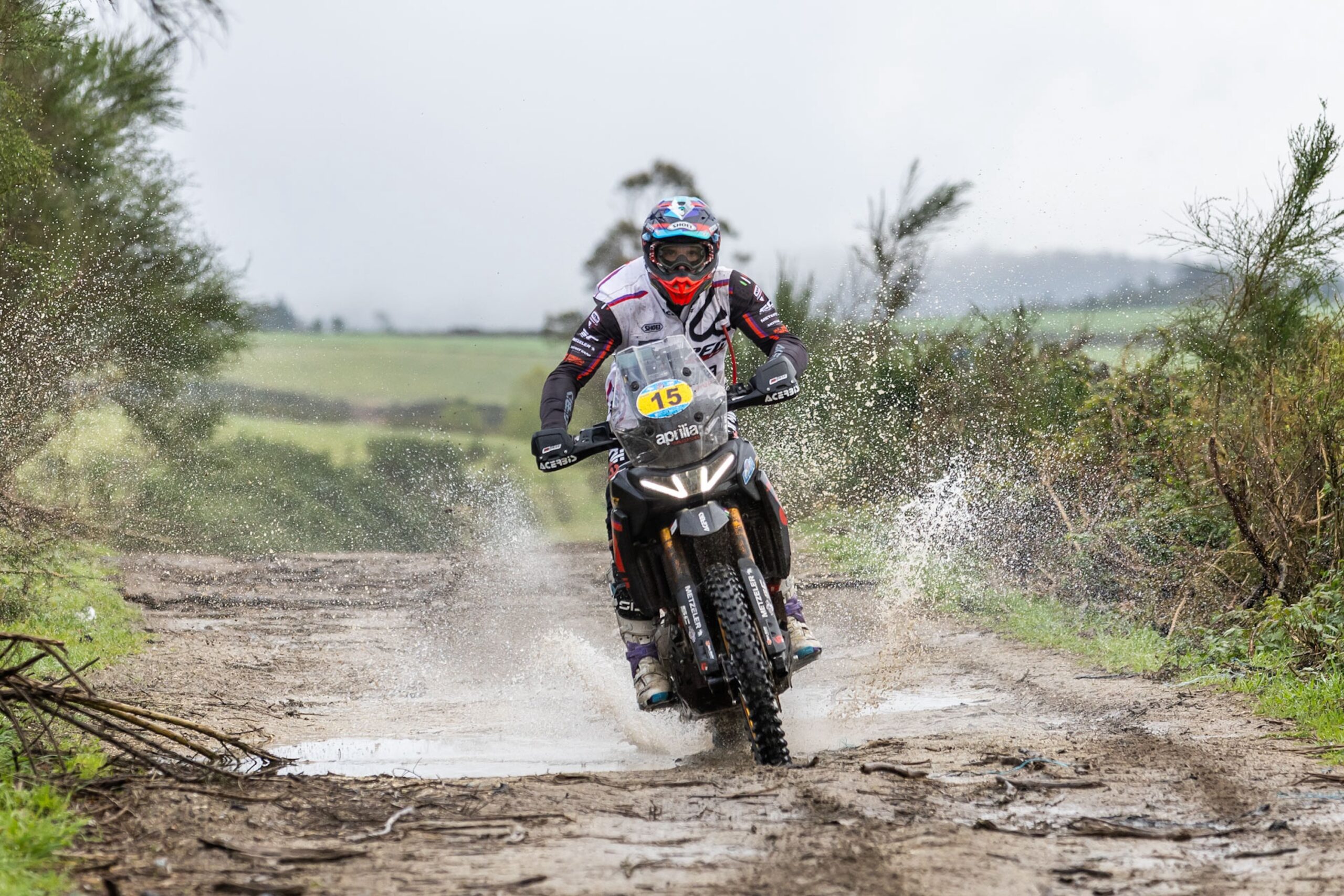 Rally rider on an Aprilia Tuareg Rally with race number 15 riding through a puddle on a dirt track