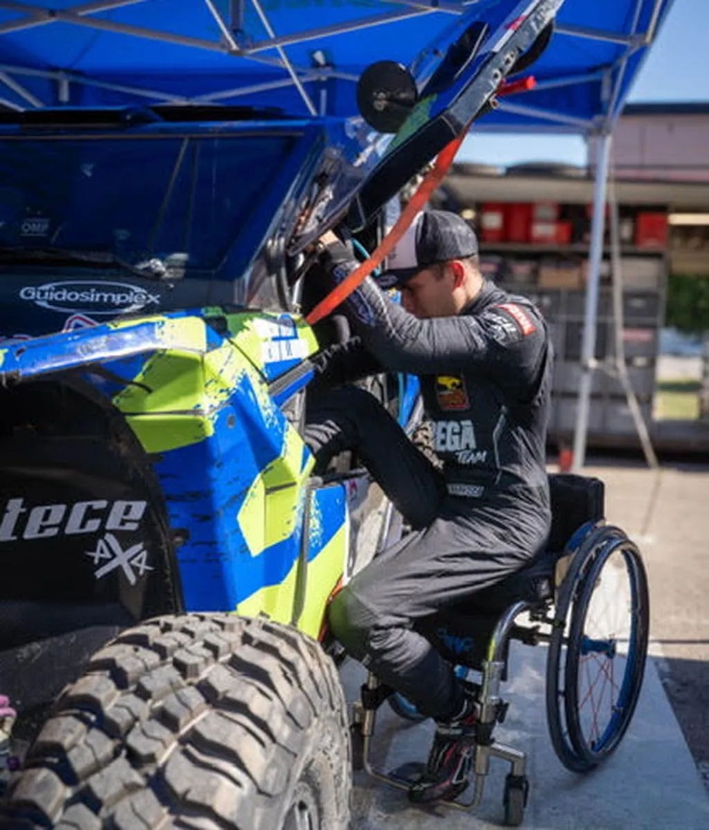 Carlos Tatay steigt aus seinem Rollstuhl in einen blau-gelben Rallye-Buggy