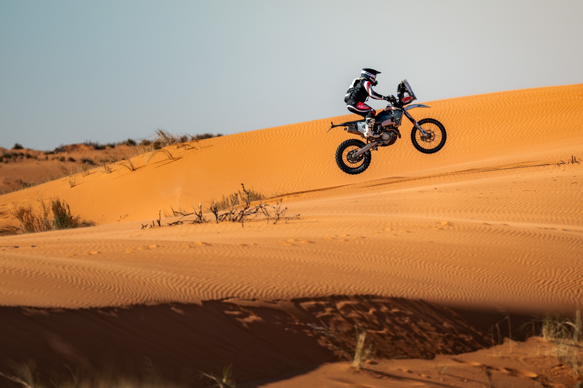 Rally motorcycle jumping over an orange sand dune