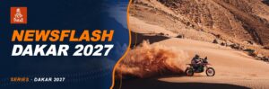 Rally motorcyclist kicking up a cloud of sand on a dune in front of a rocky mountain in Morocco