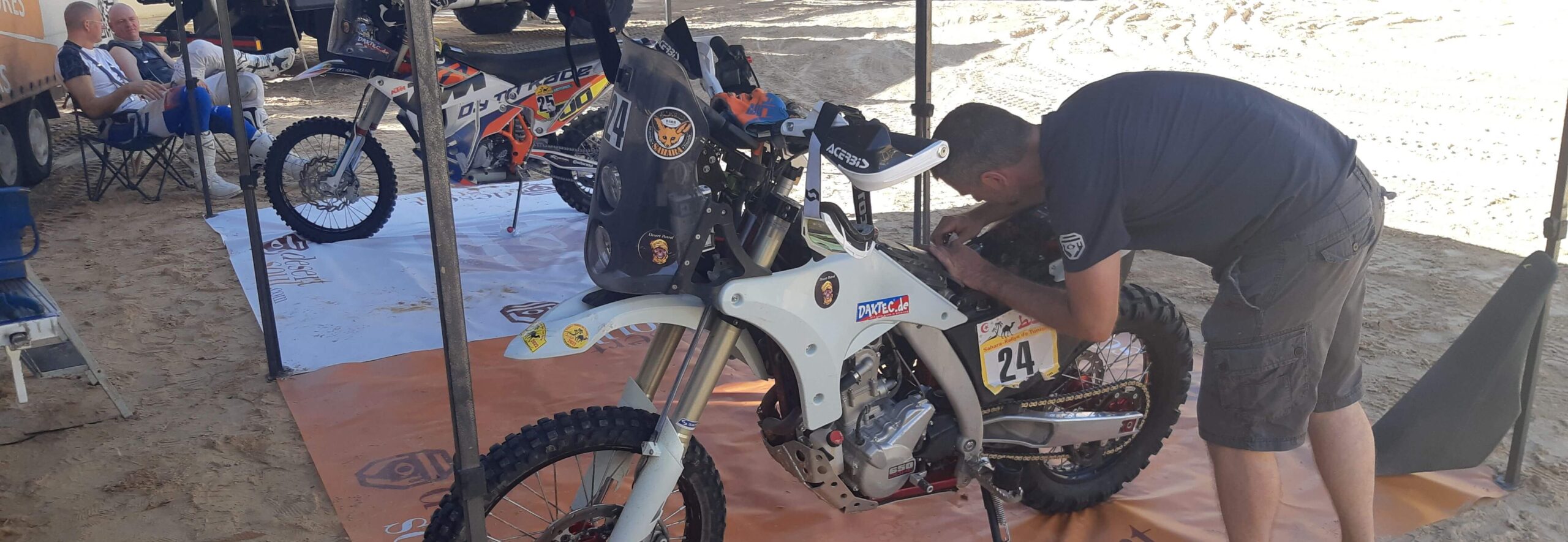 Motorcycle with race number 24 being serviced in a service tent, team equipment in the background