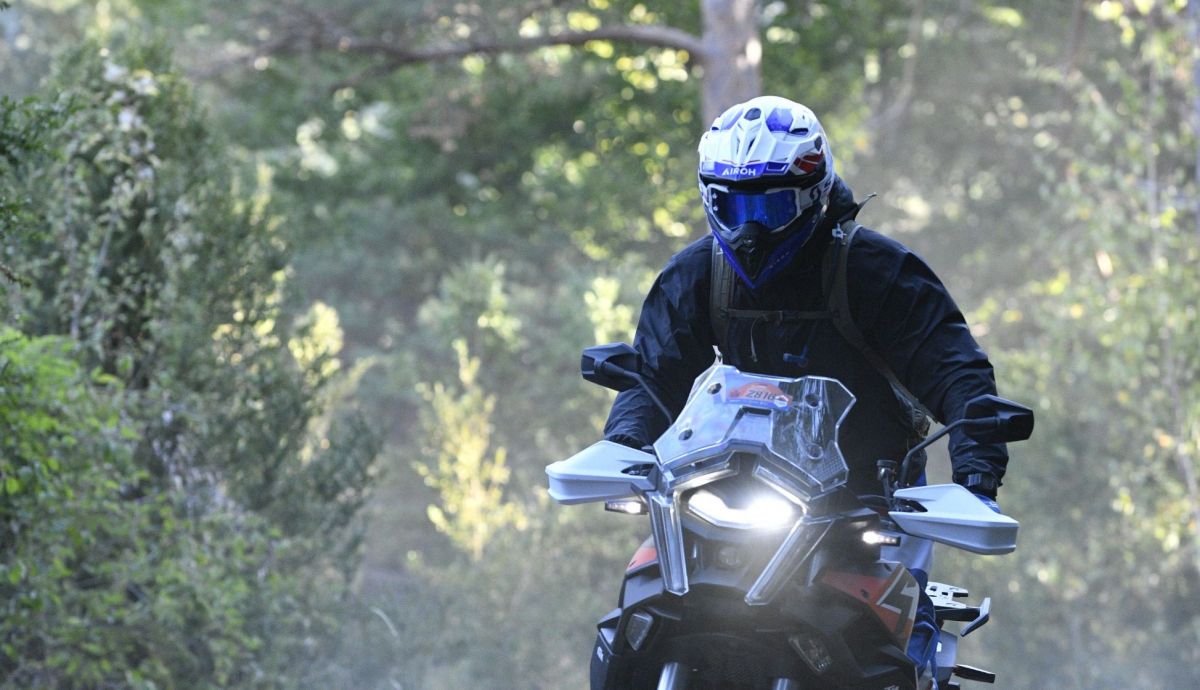 Fahrer mit wei&szlig;em Helm auf einer Reiseenduro auf einem Waldweg im Gegenlicht